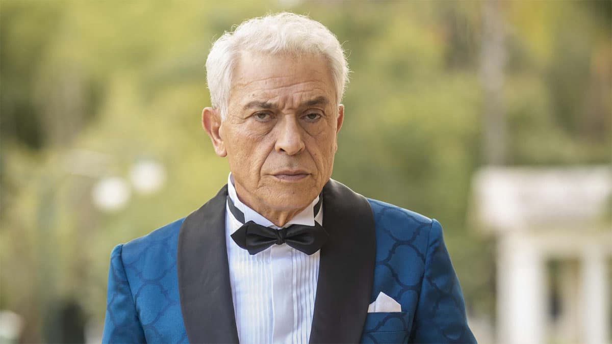 Leonel, vestido de azul e branco, sobre um fundo de árvores, na novela Amor Perfeito