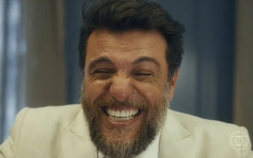 Moretti sorrindo e usando um paletó branco em cena da novela Travessia