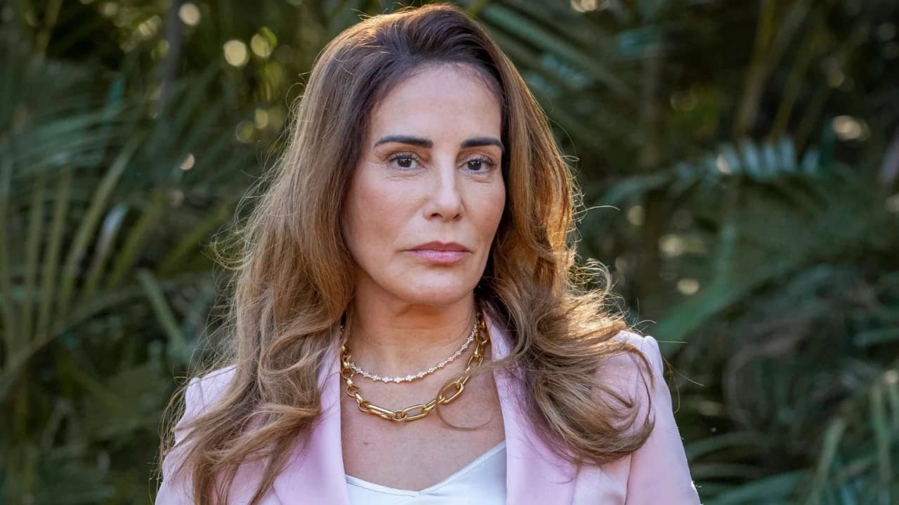 Irene, personagem de Gloria Pires, vestindo um blazer rosa, com joias no pescoço e com um olhar desafiador em Terra e Paixão.