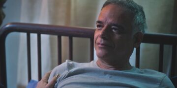 Andrade, personagem de Ângelo Antônio, com expressão de tristeza e com a cabeça encostada na cabeceira de uma cama, em Terra e Paixão.