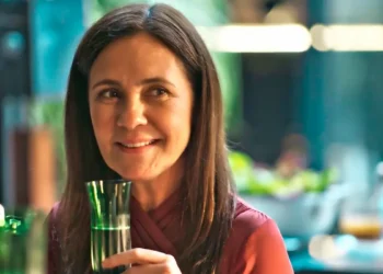 Mércia, com olhar desafiador, segurando uma taça de champanhe em cena de Mania de Você.