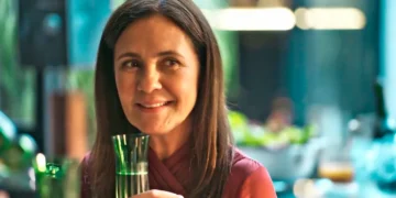 Mércia, com olhar desafiador, segurando uma taça de champanhe em cena de Mania de Você.