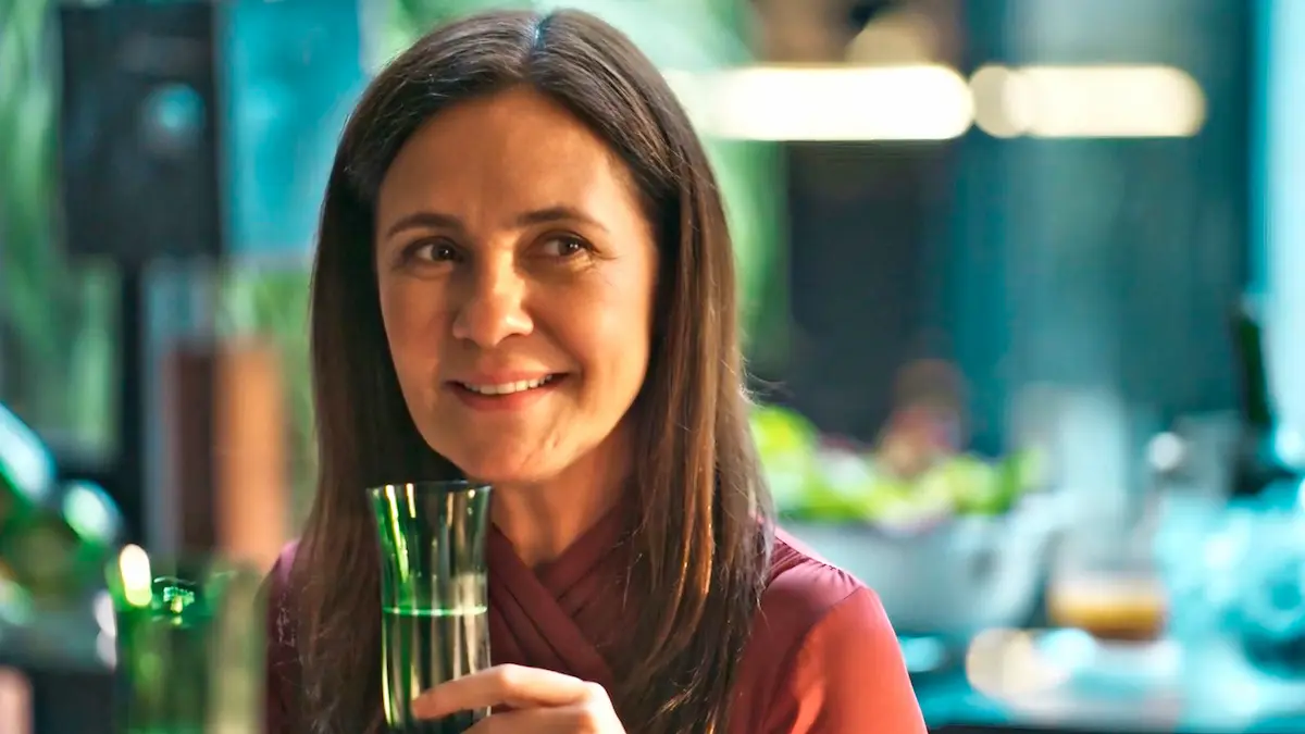 Mércia, com olhar desafiador, segurando uma taça de champanhe em cena de Mania de Você.